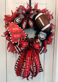 A Georgia Bulldogs themed fall wreath hanging on a white door. The wreath features red and black mesh ribbons, a football, a sign that reads 'Fall Means Football in the Soul', and a large bow with 'GEORGIA' printed on it.